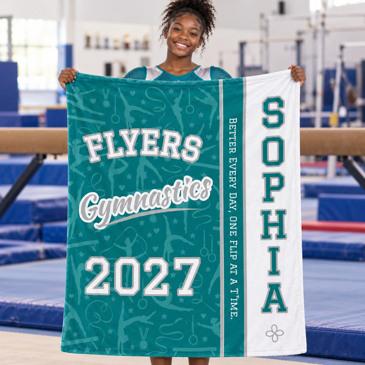 Teen gymnast holding a personalized teal varsity split Gymnastics blanket in a gym